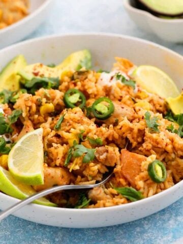 cooked chicken and rice in a white bowl topped with green peppers and avocado.