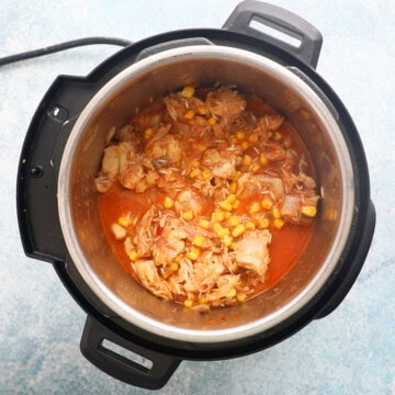 corn, raw rice and chicken along with red broth in an instant pot.