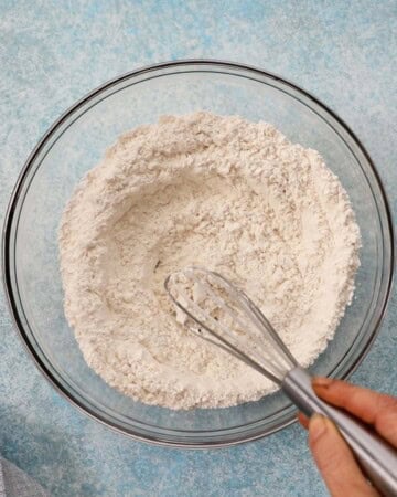 a hand whisking white flour using a whisk.