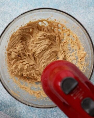 a red beater beating banana cake batter in a glass bowl.