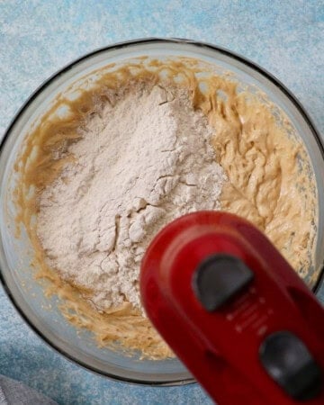 a red beater beating banana cake batter in a glass bowl.