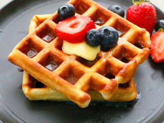 homemade Belgian waffles on a black plate topped with berries.