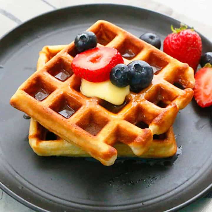 homemade Belgian waffles on a black plate topped with berries.