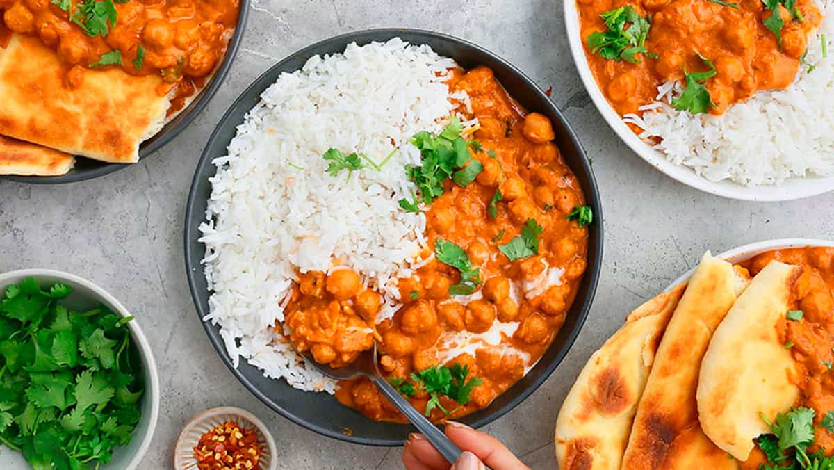 white rice and orange butter chickpeas along with a spoon in a round black plate.