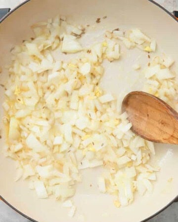 a hand cooking white onion in a white pan.