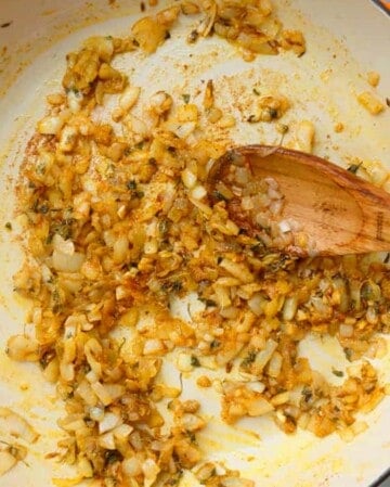 a hand cooking spicy onions in a white pan.
