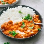 white rice and orange butter chickpeas along with a spoon in a round black plate.