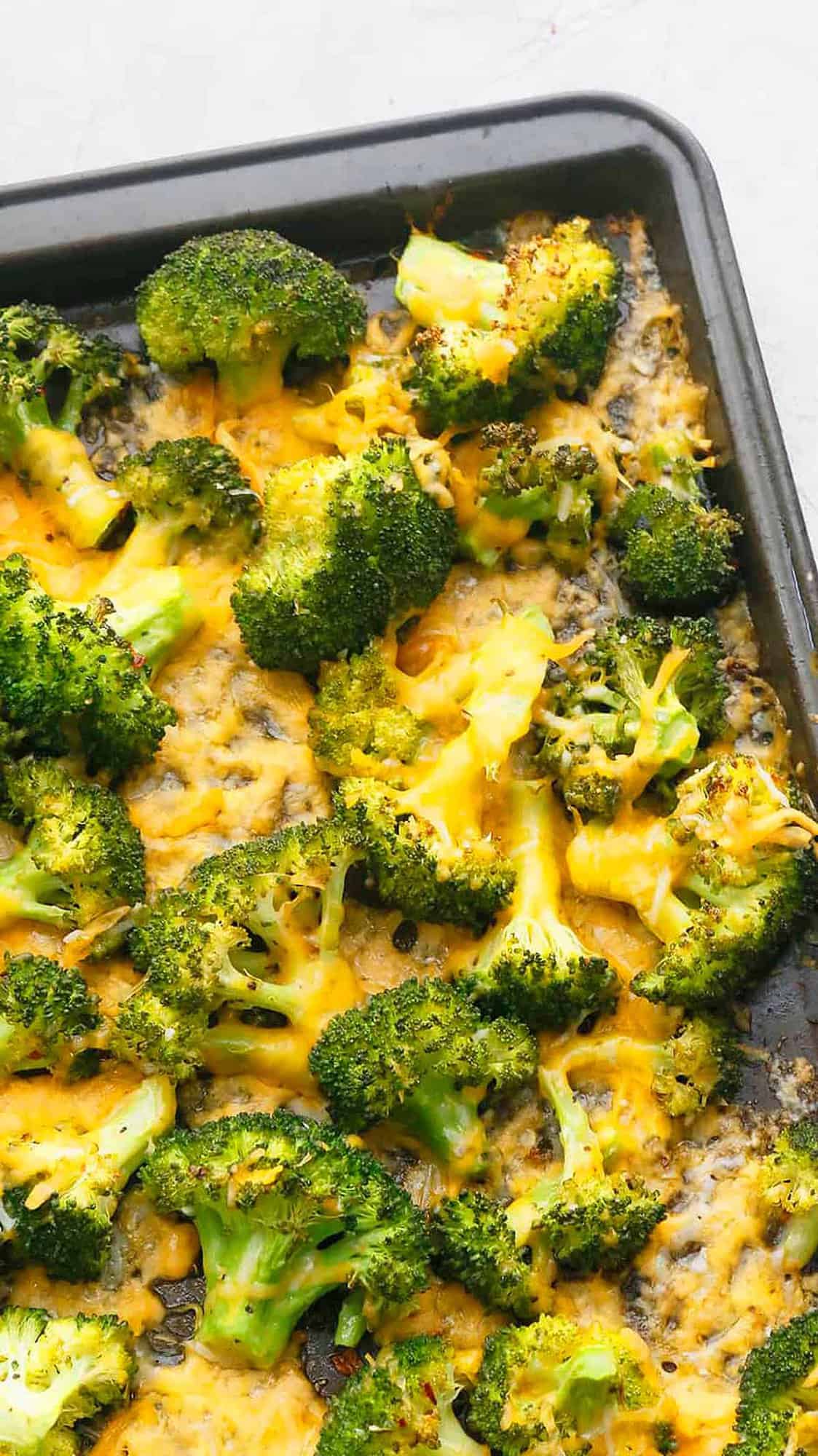 black sheet pan with broccoli and yellow melted cheese.