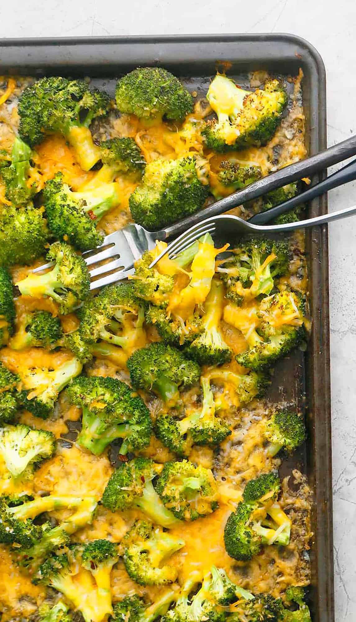 black sheet pan with broccoli and yellow melted cheese along with 2 forks.