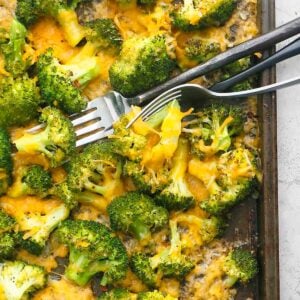 cooked broccoli with yellow cheddar cheese and two forks.