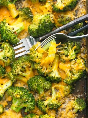 cooked broccoli with yellow cheddar cheese and two forks.