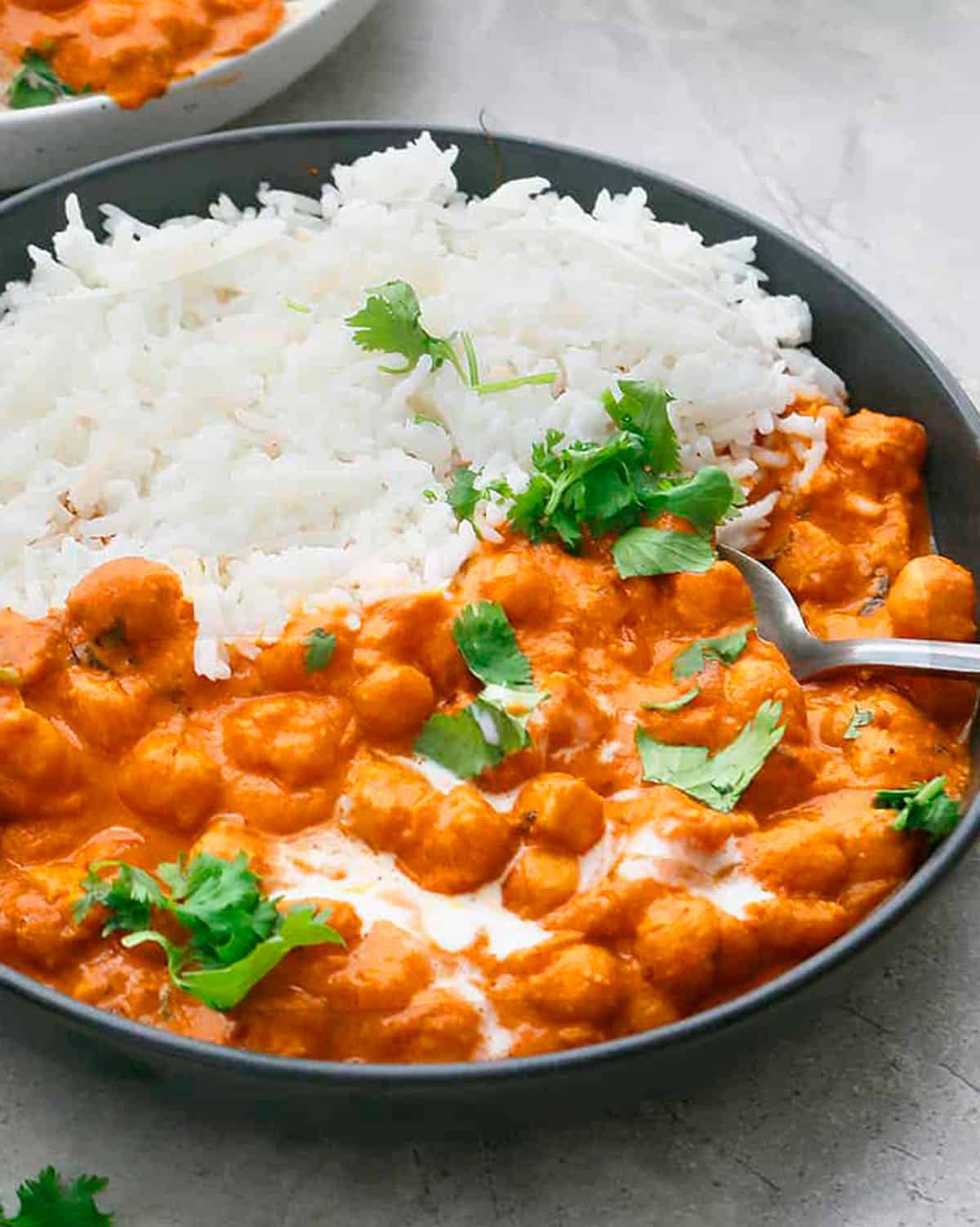 white rice and orange butter chickpeas along with a spoon in a round black plate.