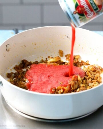red tomato sauce being poured into a white pan.