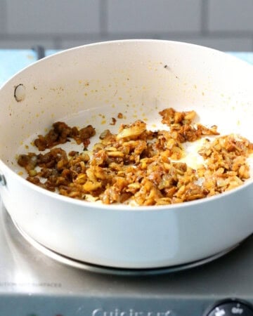 chopped onion and spices cooking in a white pan.