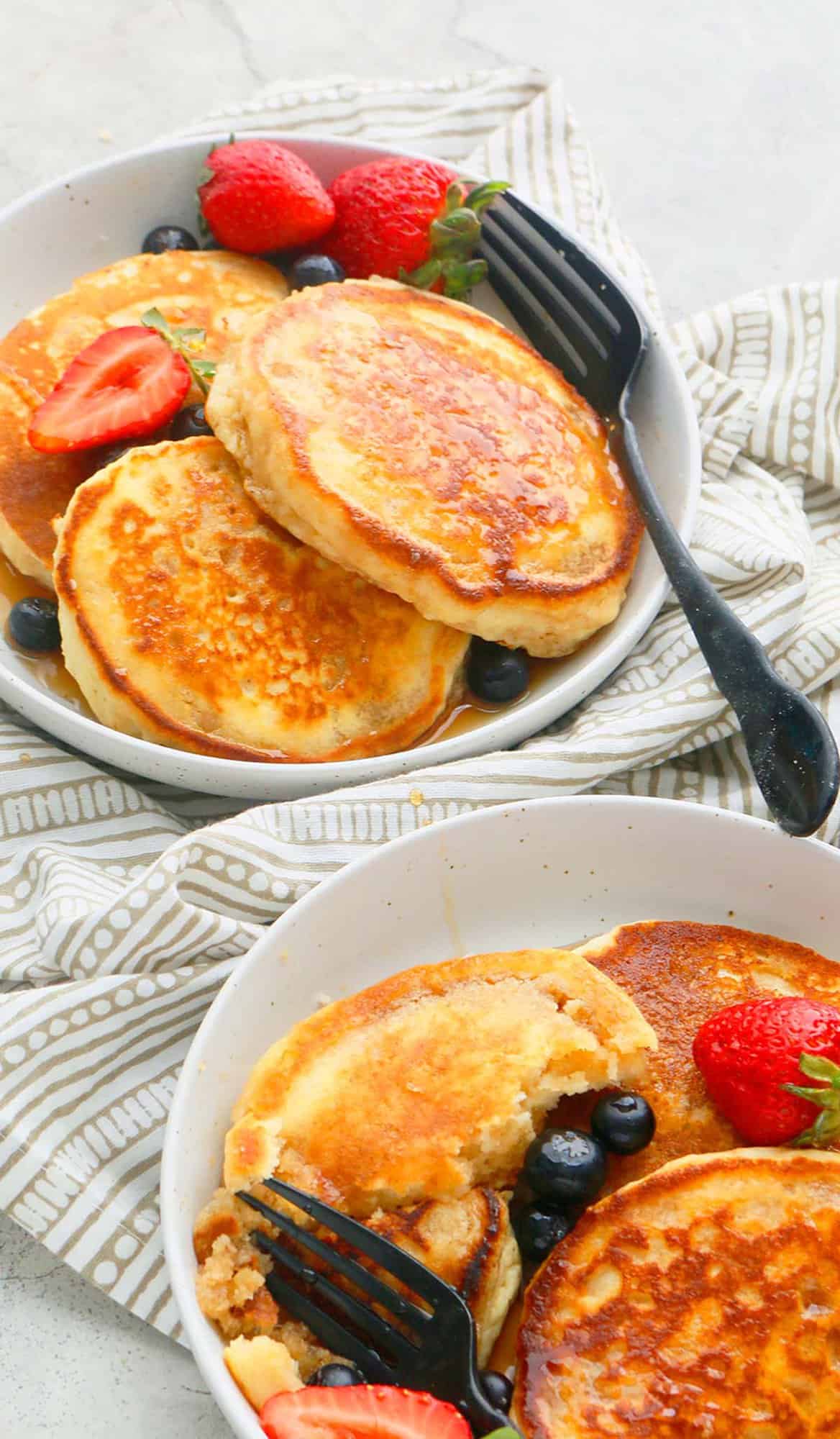 2 white bowls with thick pancakes, black fork and berries. 