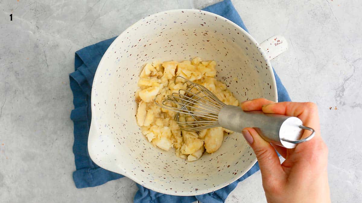 a hand mashing chopped bananas with a wire whisk. 