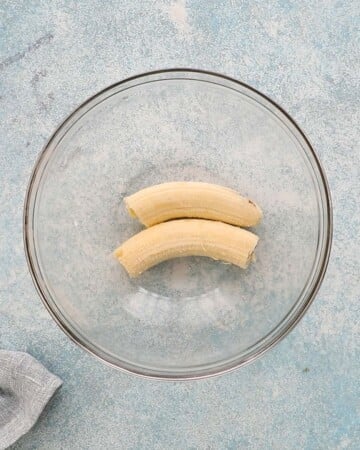two peeled bananas in a glass bowl.