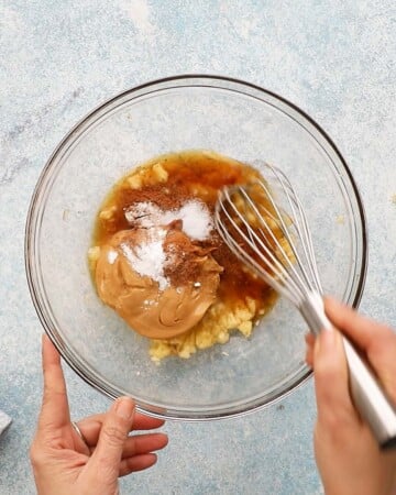 two hands mixing brown wet ingredients in a glass bowl.