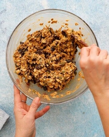 two hands mixing breakfast cookies dough in a glass bowl.