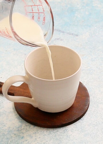 a hand pouring milk into a white mug.