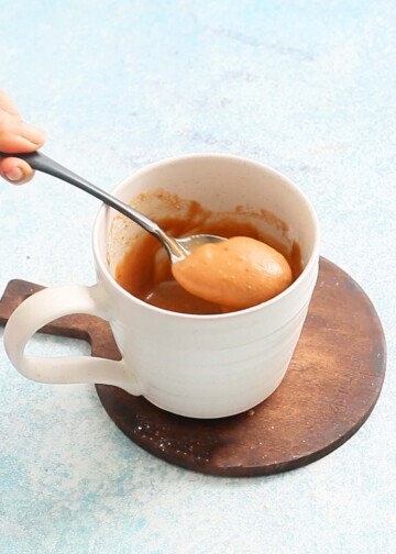 two hands stirring chai cake batter in a white mug.