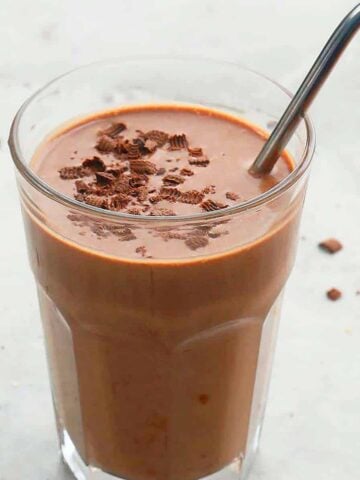 one tall glass with brown smoothie and a stainless steel straw.