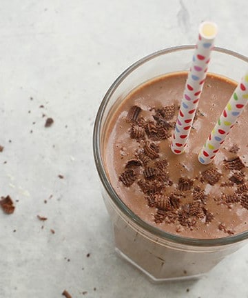 a glass filled with thick banana date smoothie, topped with chocolate shavings and 2 paper straws