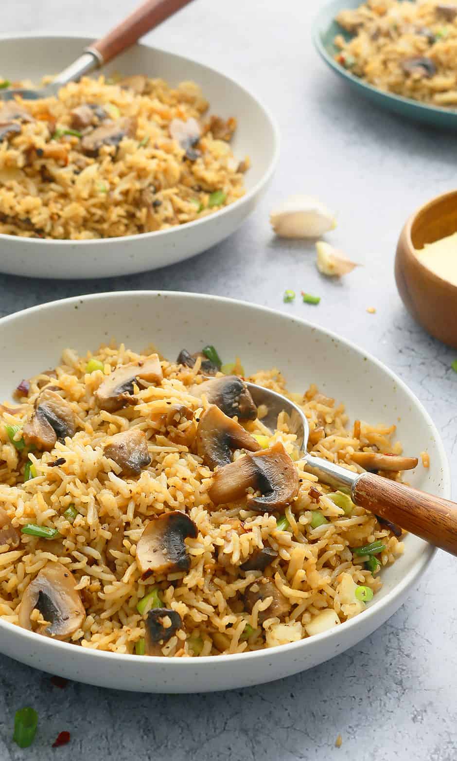 2 white bowls with cooked mushroom fried rice and spoon.