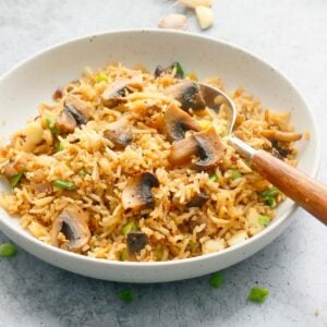 round white shallow bowl with mushroom rice and a wooden spoon.