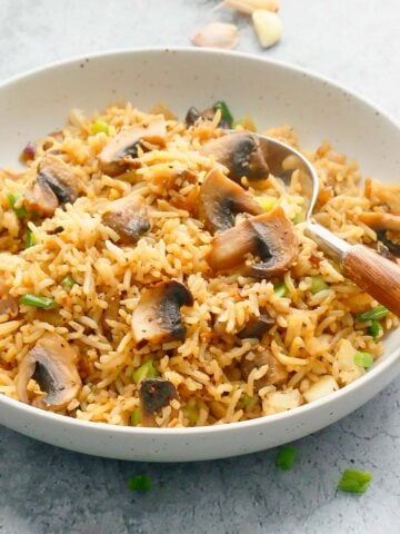 round white shallow bowl with mushroom rice and a wooden spoon.