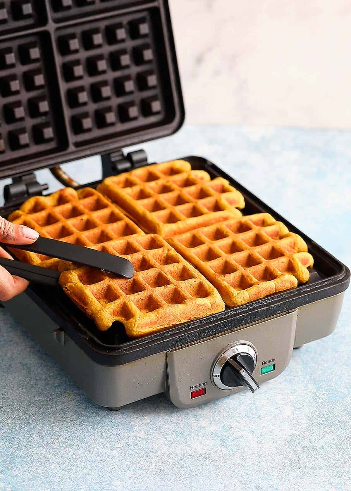 a hand removing one cooked pumpkin waffle from a waffle iron.
