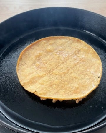 one smashed chicken taco cooking in a black skillet.