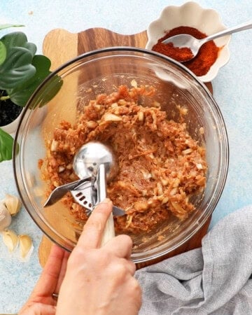 a hand scooping some ground chicken taco filling using an ice cream scoop.