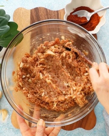 a hand mixing ground chicken taco filling in a glass bowl.