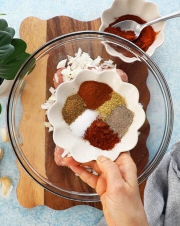 a hand holding some spices in a small white bowl.
