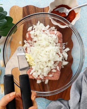 pink ground chicken and chopped onion in a glass bowl.