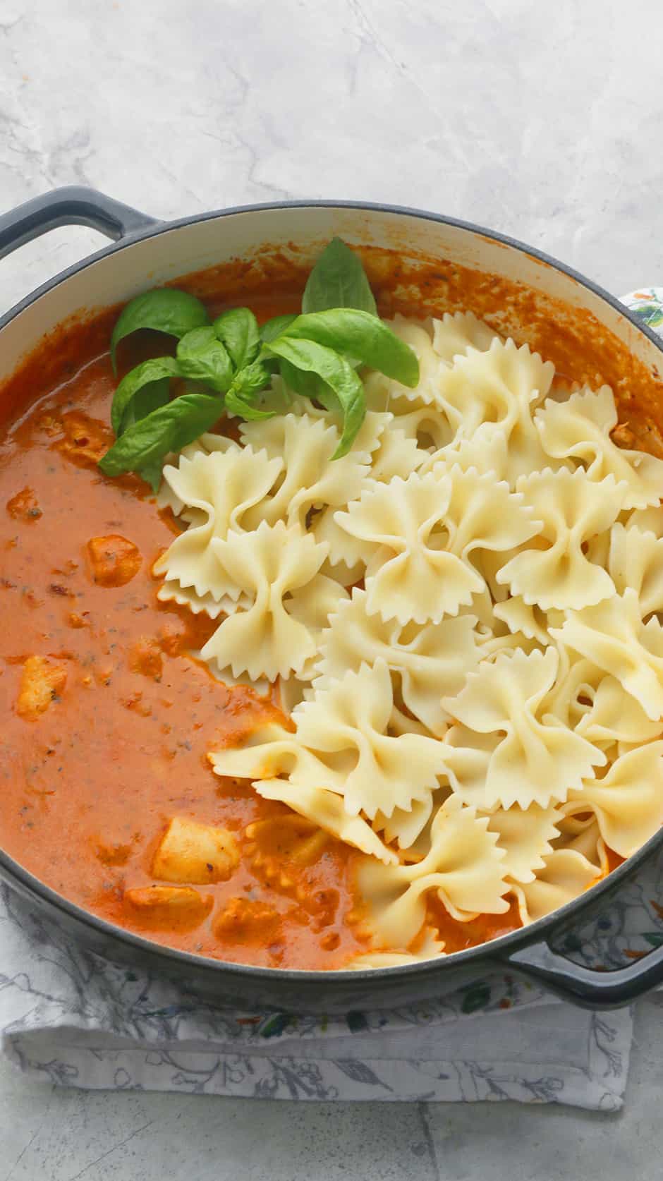 black enameled pan with spicy chicken pasta garnished with fresh basil