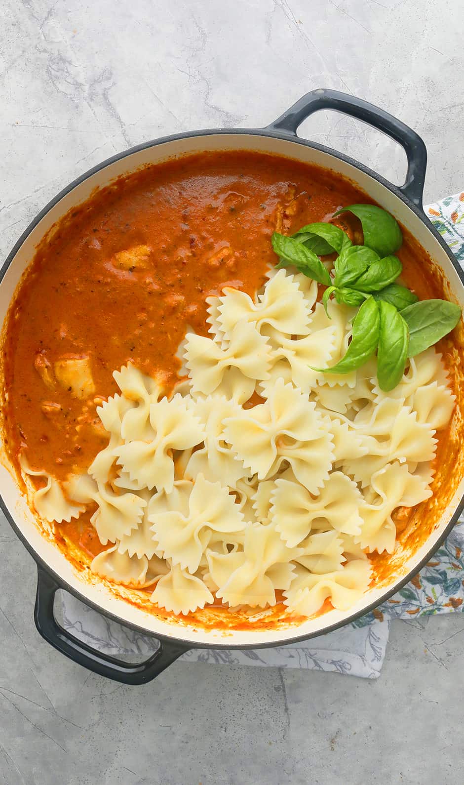 black enameled pan with spicy chicken pasta garnished with fresh basil