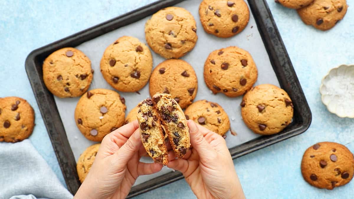 two hands holding one broken chocolate chip cookie.