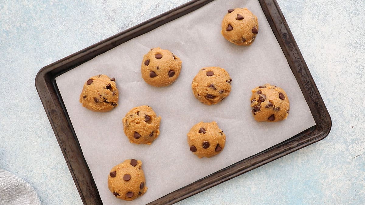shaped chocolate chip cookie dough placed on a parchment lined baking sheet.