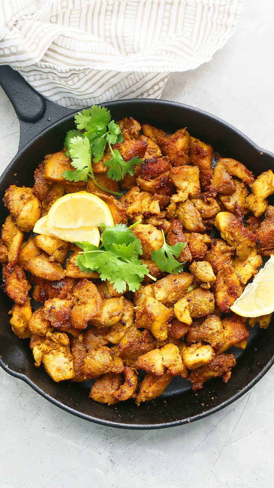 a cast iron skillet with indian spicy chicken garnished with lemon wedges and cilantro