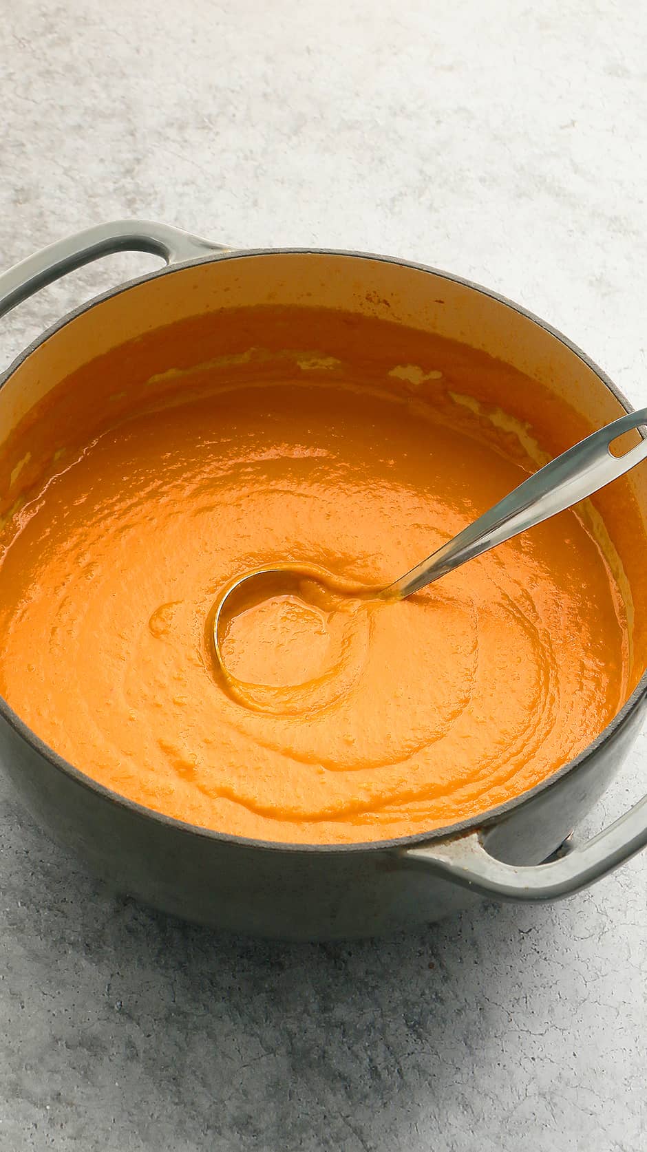 thick carrot soup in a enameled pot with a stainless steel ladle.