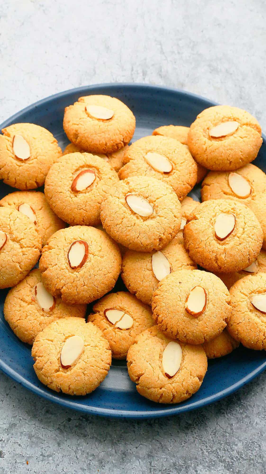 large blue plate filled with small golden colored almond cookies. 