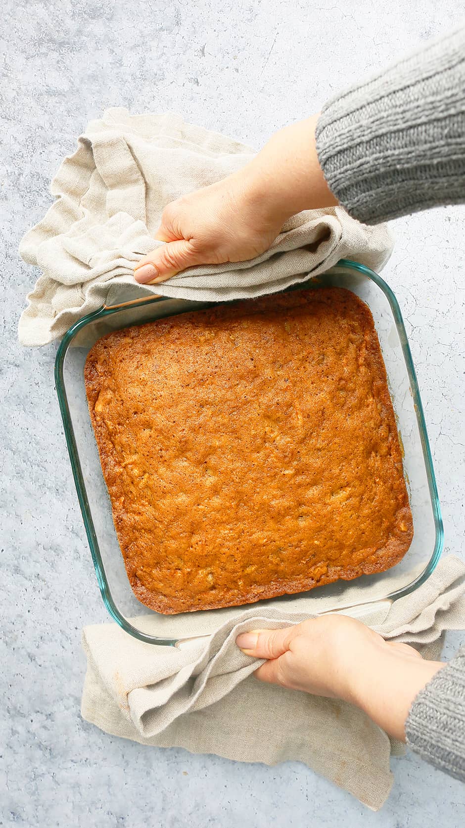 2 hands holding a hot carrot walnut cake with folded kitchen towels.