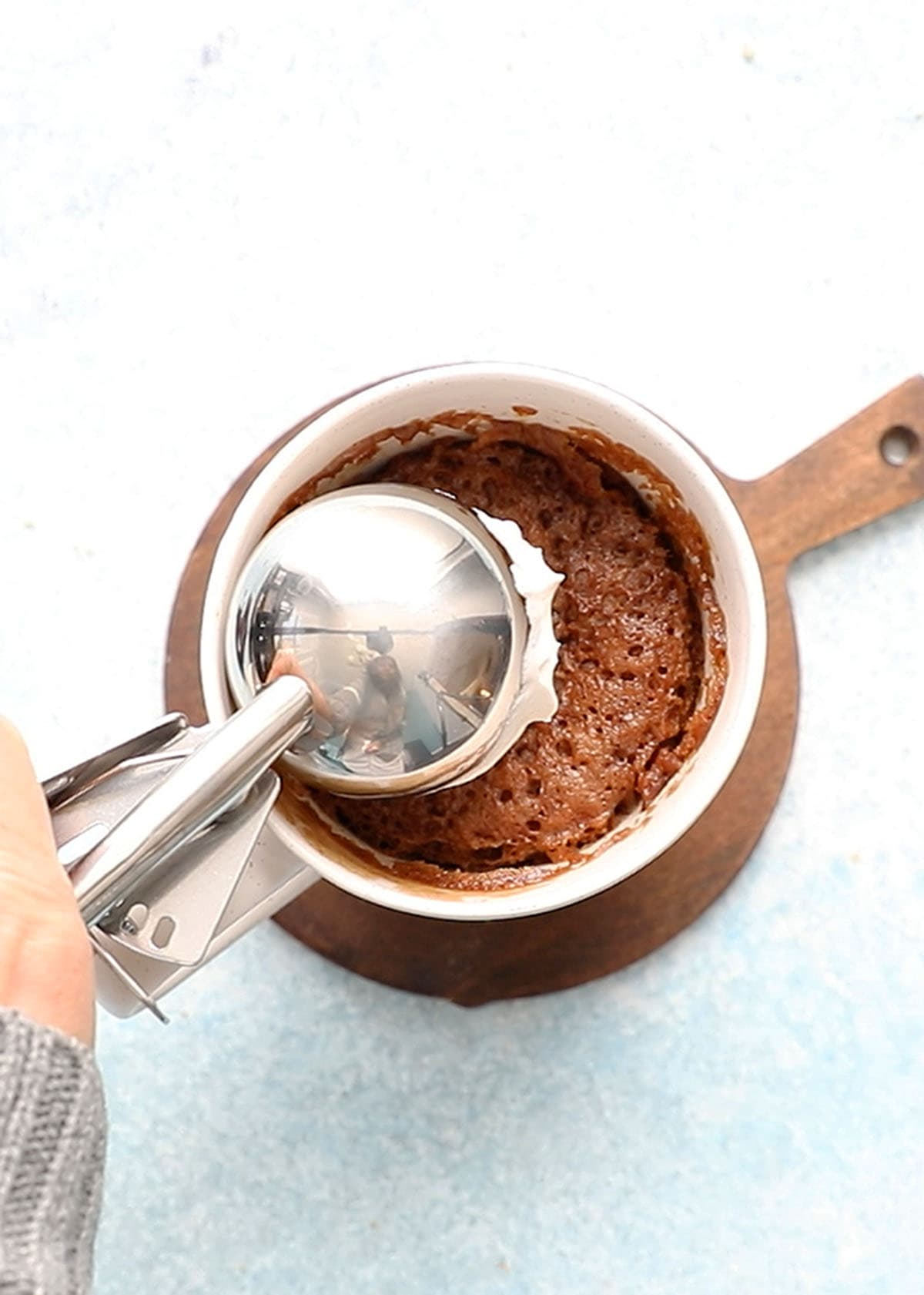 a hand adding a scoop of whipped cream on top of a mug cake.