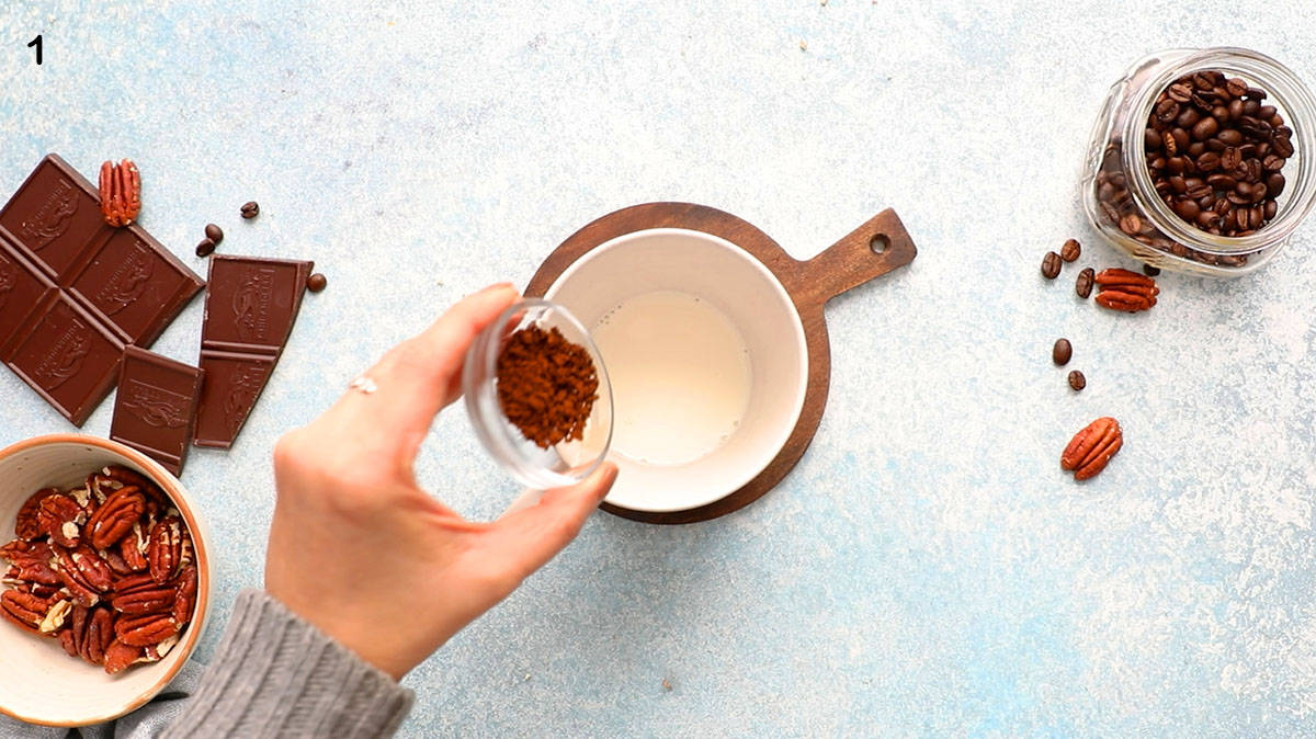a hand adding coffee granules into a white mug. 