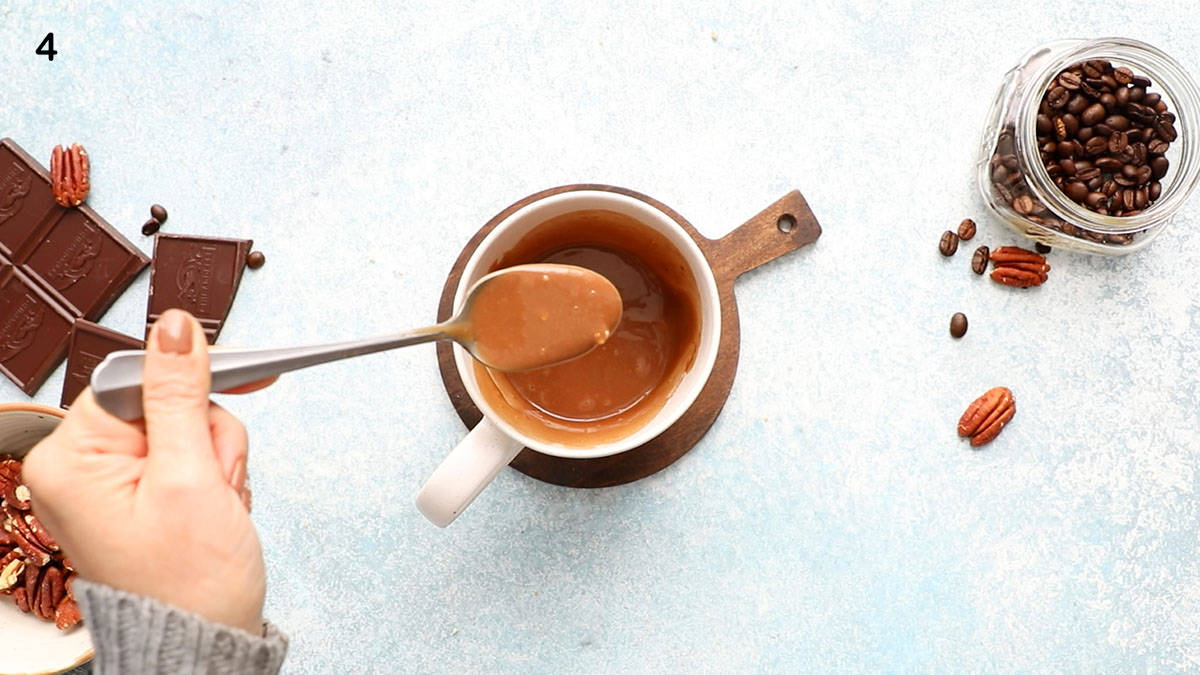 a hand stirring mocha cake batter in a white mug using a spoon.