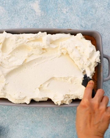 a hand spreading white whipped cream in a grey rectangular pan.
