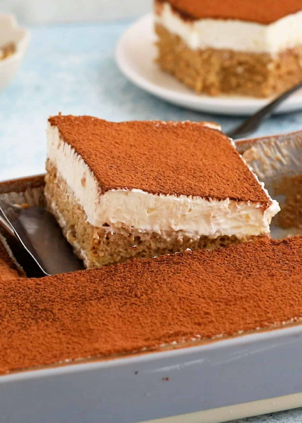 a hand removing one slice of tres leches cake from a rectangular baking pan.