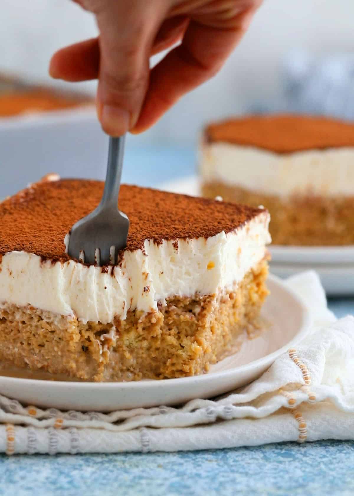 a hand cutting into a slice of tres leches cake using a black fork.
